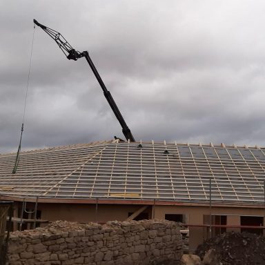 Kran hebt Materialien auf das Dach eines im Bau befindlichen Hauses unter bewölktem Himmel.