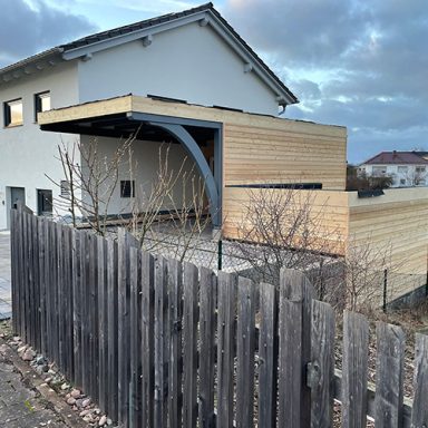 Moderne Architektur eines Hauses mit Holzverkleidung und einem überdachten Eingangsbereich und Carport.