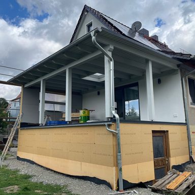 Nachträglicher Anbau einer überdachten Terrasse und holzverkleideter Außenwand.