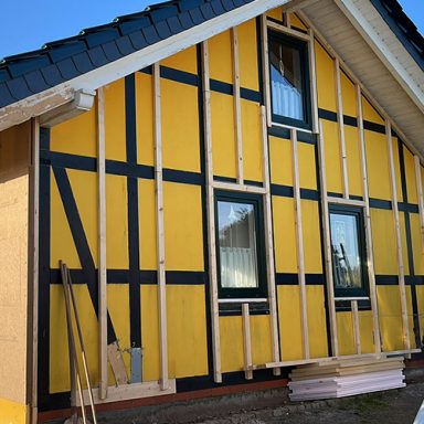 Fassade eines Hauses mit gelben Wänden und Fachwerkrahmen. Es wurde eine Konterlattung angebracht, um die Fassade nachträglich zu dämmen.