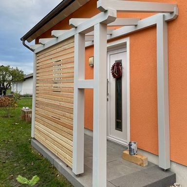 Überdachter Eingangsbereich mit Holzverkleidung und orangefarbener Hauswand.